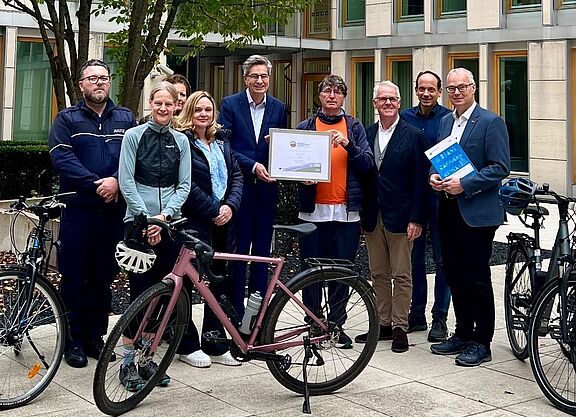 Gruppe von neun Personen steht vor dem Oberlandesgericht Düsseldorf, in der Mitte wird das gerahmte Gold-Zertifikat „Fahrradfreundlicher Arbeitgeber" präsentiert, im Vordergrund stehen drei Fahrräder.